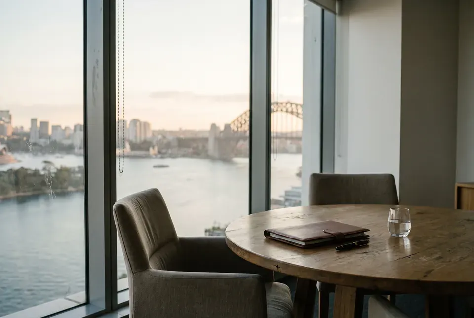 A meeting table by floor-to-ceiling windows overlooking Sydney Harbour and the Harbour Bridge